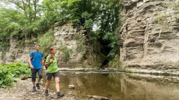 Two hikers walk past the Prümer Tor rock gate beside the Ahr river