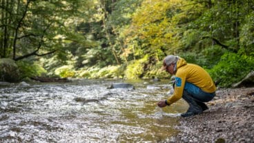 A hiker crouching by the Alb River on the Albsteig Schwarzwald cupping water in his hands