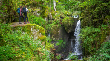 Two hikers standing on a rock above the Höllbach waterfalls