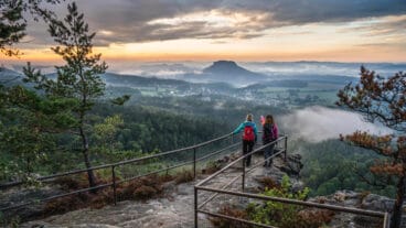 Two hikers watch the sunset from a viewpoint of the Papststein