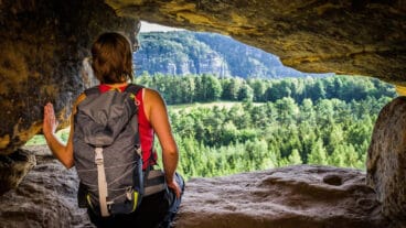 A hiker looks out from a cave on the Rauenstein onto the forest beyond