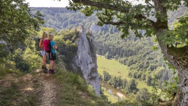 Two hikers standing at the top of the Stiegelesfelsen looking into the Danube valley with river below