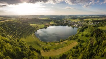 An aerial view of the Schalkenmehrener volcanic crater lake with Schalkenmehren village beside it