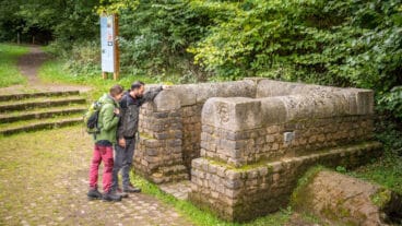 Two hikers look into the Roman ruins of the Grüner Pütz spring collection facility