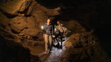 Two hikers with flashlights explore the Mühlsteinhöhle cave in the Rother Kopf